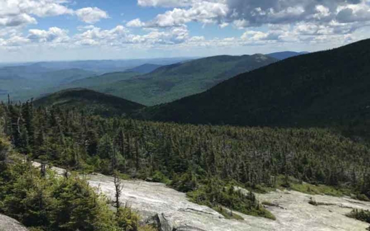 the Appalachian mountains of maine appear vast and green below a blue sky dotted with clouds